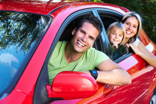 Family leaning out the window of a red car